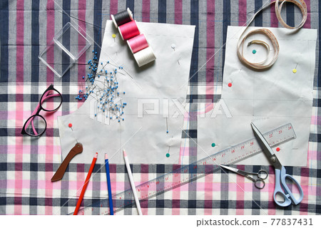 Sewing supplies on a draft paper of pants on fabric, sewing thread, scissors, , colorful pen, pencil, ruler, centimeter tape, spool of thread and equipment Sewing supplies on a draft paper of pants on fabric, sewing thread, scissors, , colorful pen, pencil, ruler, centimeter tape, spool of thread and equipment 77837431