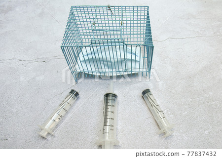 a syringe around protection mask in blue steel cage on cement floor, a concept of vaccination coming hope for covid 19 no need a mask anymore a syringe around protection mask in blue steel cage on cement floor, a concept of vaccination coming hope for covid 19 no need a mask anymore 77837432