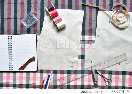 Sewing supplies on a draft paper of pants on fabric, sewing thread, scissors, , colorful pen, pencil, ruler, centimeter tape, spool of thread and equipment 77837459