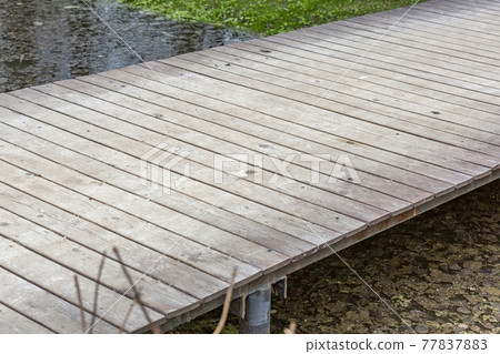 Narrow wooden footbridge over the stream in the park at daytime Narrow wooden footbridge over the stream in the park at daytime 77837883