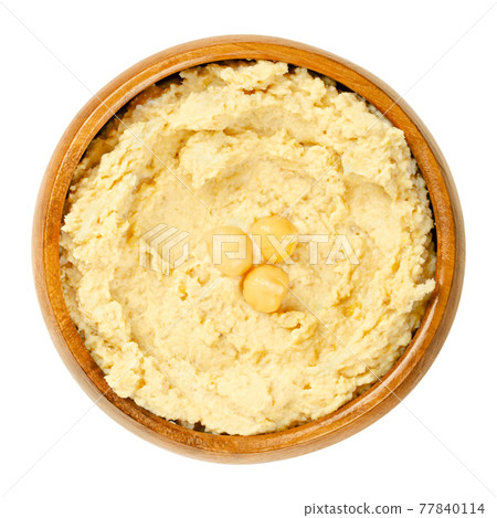 Hummus dip with chickpea garnish, in a wooden bowl. Middle Eastern dip, spread or savory dish made of cooked, mashed chickpeas, blended with tahini, lemon juice and garlic. Close-up, macro food photo. Hummus dip with chickpea garnish, in a wooden bowl. Middle Eastern dip, spread or savory dish made of cooked, mashed chickpeas, blended with tahini, lemon juice and garlic. Close-up, macro food photo. 77840114