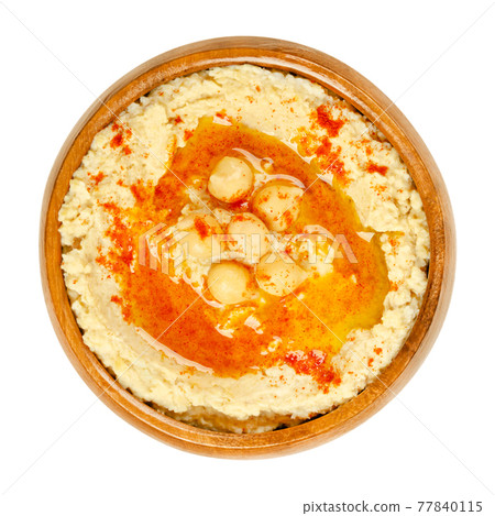 Hummus dip with paprika powder and oil, in a wooden bowl. Middle Eastern dip, spread or savory dish made of cooked, mashed chickpeas, blended with tahini, lemon juice and garlic. Close-up, food photo. 77840115