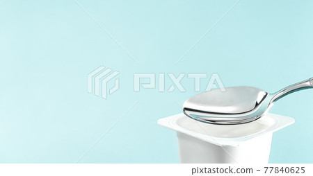 Yogurt cup and silver spoon on mint background, white plastic container with yoghurt cream, fresh dairy product for healthy diet and nutrition balance 77840625
