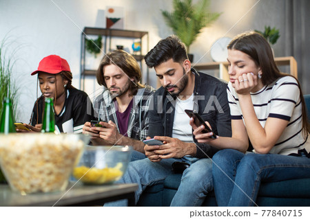 Multi ethnic friends using personal smartphones on couch 77840715