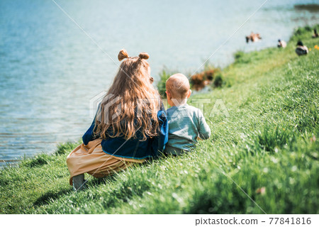 Two adorable sisters feeding ducks by a river at summer 77841816