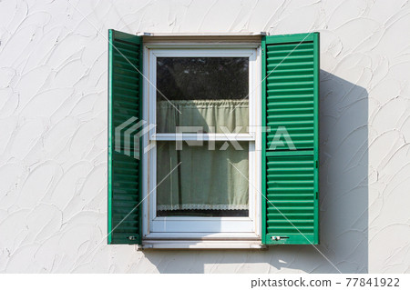 Sunlit white-walled glass windows and green wooden shutters and shadows 77841922