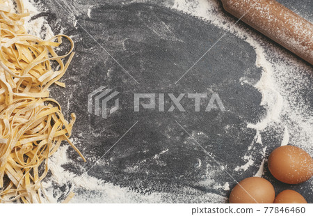 Making homemade background pasta. Kitchen table background with flour, pasta, rolling pin and eggs for making dough and Italian pasta or egg noodles. 77846460