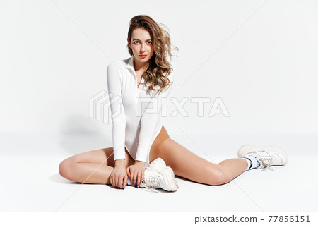 Sexy sporty woman in white bodysuit posing on white studio background Sexy sporty woman in white bodysuit posing on white studio background 77856151