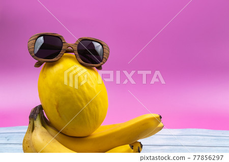An assortment of yellow fruits and glasses lies on a pink background 77856297