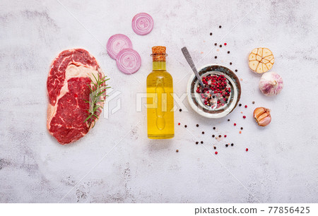 Raw Rib Eye Steak set up on white concrete background. Flat Lay of fresh raw beef steak with rosemary and spice on white shabby concrete background top view. Raw Rib Eye Steak set up on white concrete background. Flat Lay of fresh raw beef steak with rosemary and spice on white shabby concrete background top view. 77856425