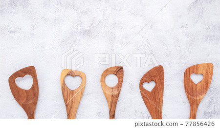 Various heart shape of wooden cooking utensils. Wooden spoons and wooden spatula on white concrete background with flat lay and copy space. 77856426
