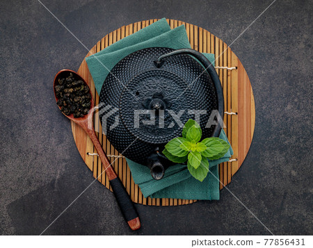 Black cast iron tea pot with herbal tea set up on dark stone background. 77856431
