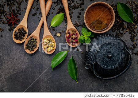 Black cast iron tea pot with herbal tea set up on dark stone background. 77856432