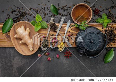 Black cast iron tea pot with herbal tea set up on dark stone background. Black cast iron tea pot with herbal tea set up on dark stone background. 77856433