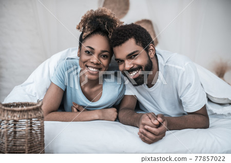 Dark skinned husband and wife lying on bed 77857022