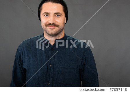 Happy hipster guy looks at camera with smile on dark background, copy space Happy hipster guy looks at camera with smile on dark background, copy space 77857148