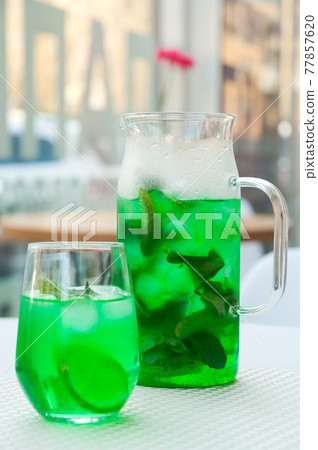cold green mint lemonade in a decanter and in a glass 77857620
