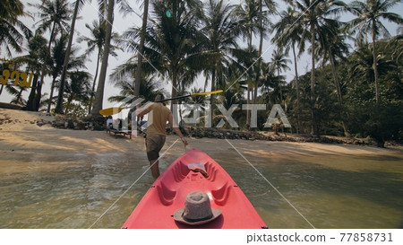 Man with sunglasses and hat rows pink plastic canoe along sea against green hilly islands with wild jungles. Traveling to tropical countries. Man with sunglasses and hat rows pink plastic canoe along sea against green hilly islands with wild jungles. Traveling to tropical countries. 77858731