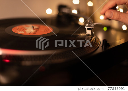 man's hands put needle on record on turntable close up. 77858991