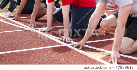 Arms and hands of four boys on their mark at the starting line on a red track 77859612