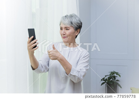 一位銀髮族年長婦女講手機電話,享受悠閒自在的生活 一位銀髮族年長婦女講手機電話,享受悠閒自在的生活 77859778
