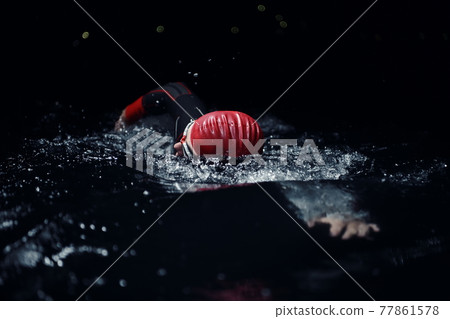 triathlon athlete swimming in dark night wearing wetsuit 77861578