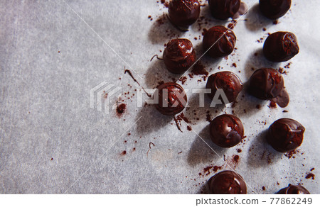 Flat lay with chocolate truffles dipped in melted chocolate mass and sparkled with cocoa powder on a baking white paper Flat lay with chocolate truffles dipped in melted chocolate mass and sparkled with cocoa powder on a baking white paper 77862249