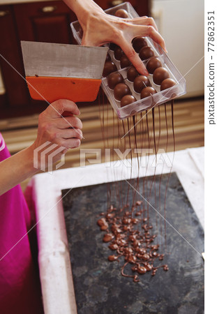 Closeup of using cake scraper to remove excess chocolate from molds into a marble table to make candy shells. Making luxury pralines and truffles at home Closeup of using cake scraper to remove excess chocolate from molds into a marble table to make candy shells. Making luxury pralines and truffles at home 77862351