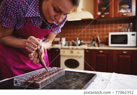 Chef pastry squeezing sweet creamy liquid from confectionery bag into candy molds for making luxury pralines and truffles at home Chef pastry squeezing sweet creamy liquid from confectionery bag into candy molds for making luxury pralines and truffles at home 77862352