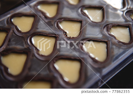 Closeup of chocolate molds in the shape of hearts full of sweet creamy filling Closeup of chocolate molds in the shape of hearts full of sweet creamy filling 77862355