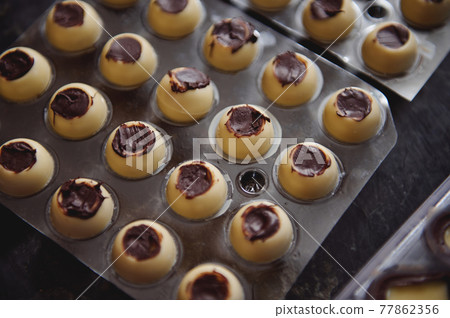 Closeup of manufacturing chocolate truffles. Spherical molds of white chocolate full of dark chocolate filling . 77862356
