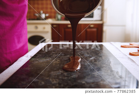 Close-up of confectioner pouring chocolate mass into marble surface for tempering. Close-up of confectioner pouring chocolate mass into marble surface for tempering. 77862385