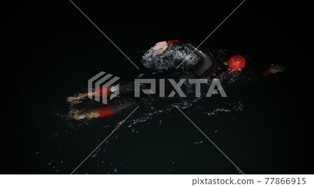 triathlon athlete swimming in dark night wearing wetsuit 77866915