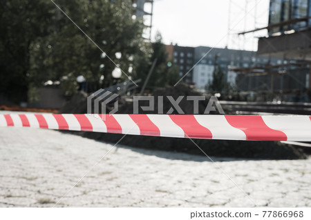 Red and white lines of barrier tape warning of danger during the construction and repair of buildings. Red and white warning Tape pole guard protects against penetration Red and white lines of barrier tape warning of danger during the construction and repair of buildings. Red and white warning Tape pole guard protects against penetration 77866968