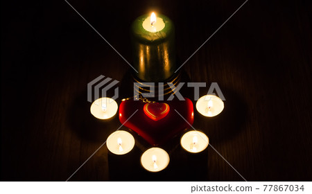 A red heart stands against a background of lighted candles. I love you. Christmas fortune telling and fortune telling. Greeting card for Valentine's day or international women's day A red heart stands against a background of lighted candles. I love you. Christmas fortune telling and fortune telling. Greeting card for Valentine's day or international women's day 77867034