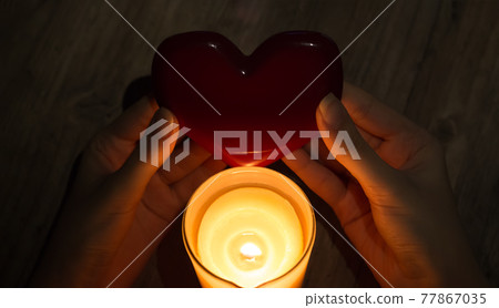 A fortune teller holds a heart in her hands and guesses at future love with a lighted candle. Christmas fortune telling and fortune telling. Red heart in the hands of a girl with a burning candle. A fortune teller holds a heart in her hands and guesses at future love with a lighted candle. Christmas fortune telling and fortune telling. Red heart in the hands of a girl with a burning candle. 77867035
