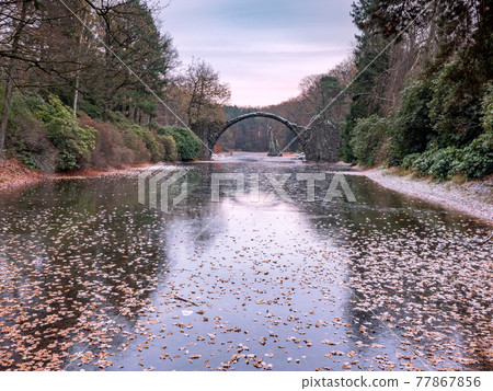 Chill autumn morning in park Kromlau. Round Arch basalt bridge Chill autumn morning in park Kromlau. Round Arch basalt bridge 77867856