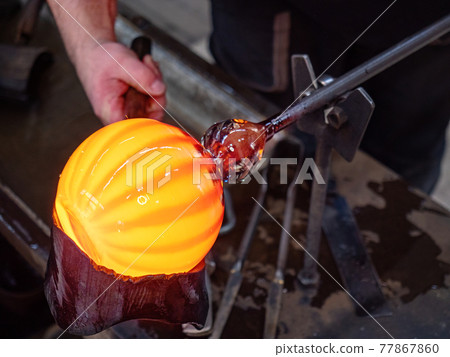 Glassblowing crafter rounds the hot-striped vase  with wet woode tool 77867860