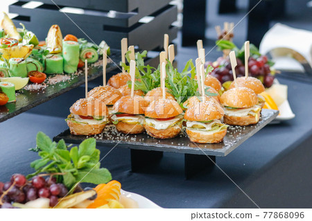 Set of several burgers for catering. Burgers on a black plate on the buffet table. 77868096