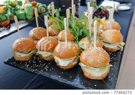 Set of several burgers for catering. Burgers on a black plate on the buffet table. 77868273