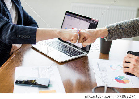 Close up of young businessman and businesswoman making a fist bump on building background. Business people wear suit do a fist pump together after good deal. Business success and teamwork concept. 77868274