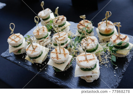 Set of several burgers for catering. Burgers on a black plate on the buffet table. 77868278