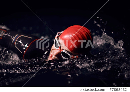 triathlon athlete swimming in dark night wearing wetsuit 77868482