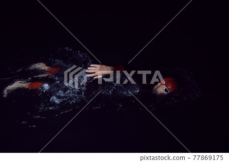 triathlon athlete swimming in dark night wearing wetsuit triathlon athlete swimming in dark night wearing wetsuit 77869175