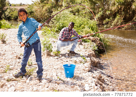Boy pulling fish from river Boy pulling fish from river 77871772