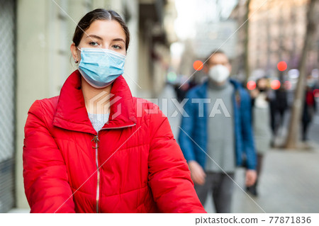 Young woman wearing face mask walks along city street Young woman wearing face mask walks along city street 77871836