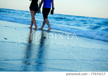 A couple walking along the beach A couple walking along the beach 77874217