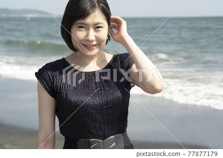 A young woman walking along the beach while being blown by the sea breeze (Shichirigahama, Kamakura City, Kanagawa Prefecture) 77877179