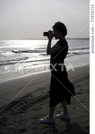 Camera girl (silhouette) shooting with a digital camera on a sandy beach 77878153