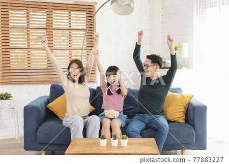 Happy Asian family eating popcorn and watching tv together on sofa at home living room. leisure and people concept 77883227